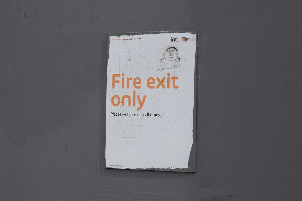 Green running-man fire exit sign in a UK commercial building
