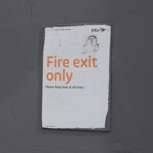 Green running-man fire exit sign in a UK commercial building